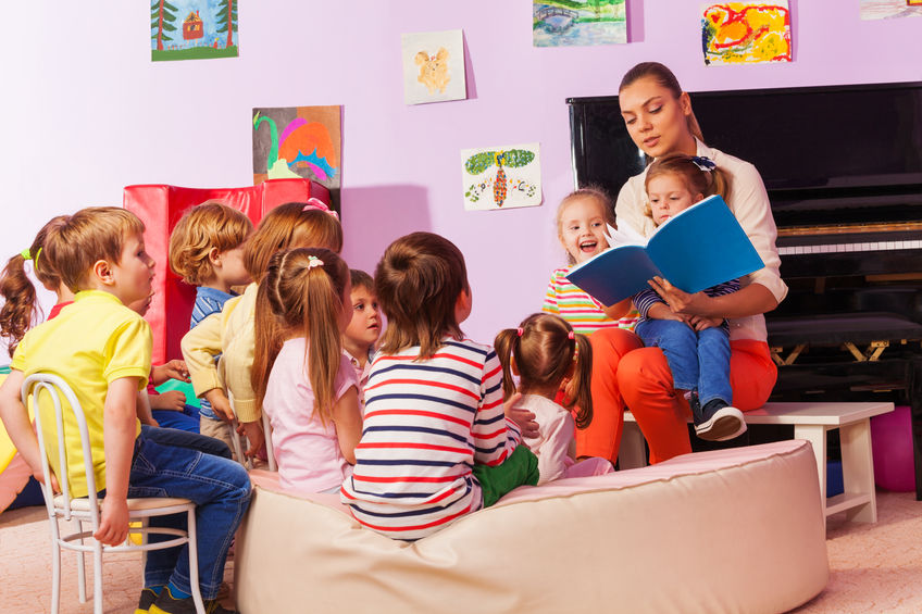 preschool kids sitting in group listening to teacher read