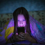 little girl in bed staring at smartphone