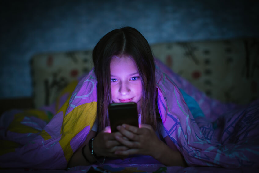 little girl in bed staring at smartphone