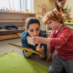 Teacher and boy playing with wooden boards on floor in school