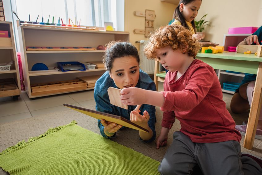 Teacher and boy playing with wooden boards on floor in school