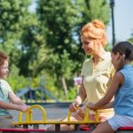 Cheerful woman riding seesaw with children in summer park