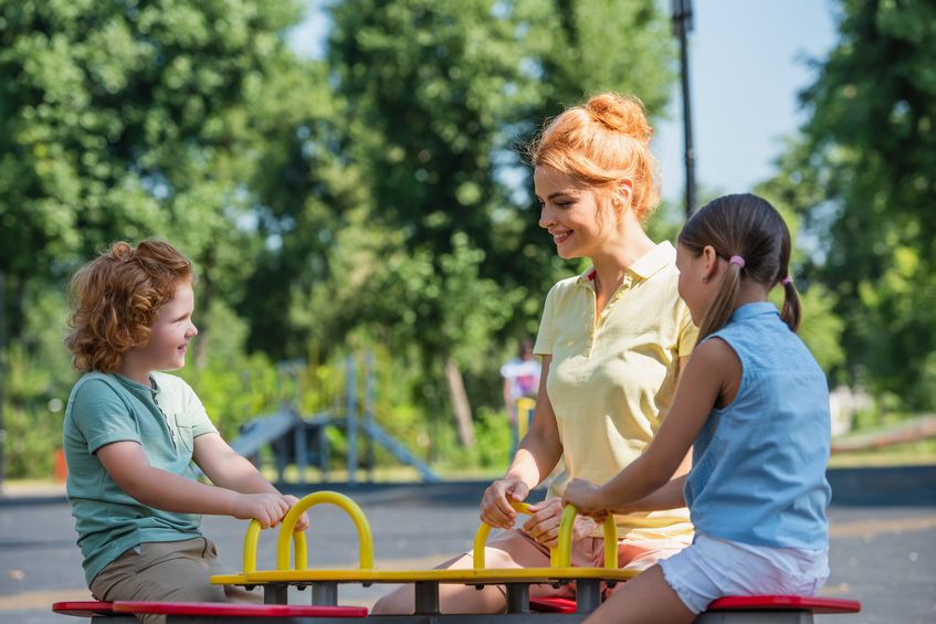 Cheerful woman riding seesaw with children in summer park